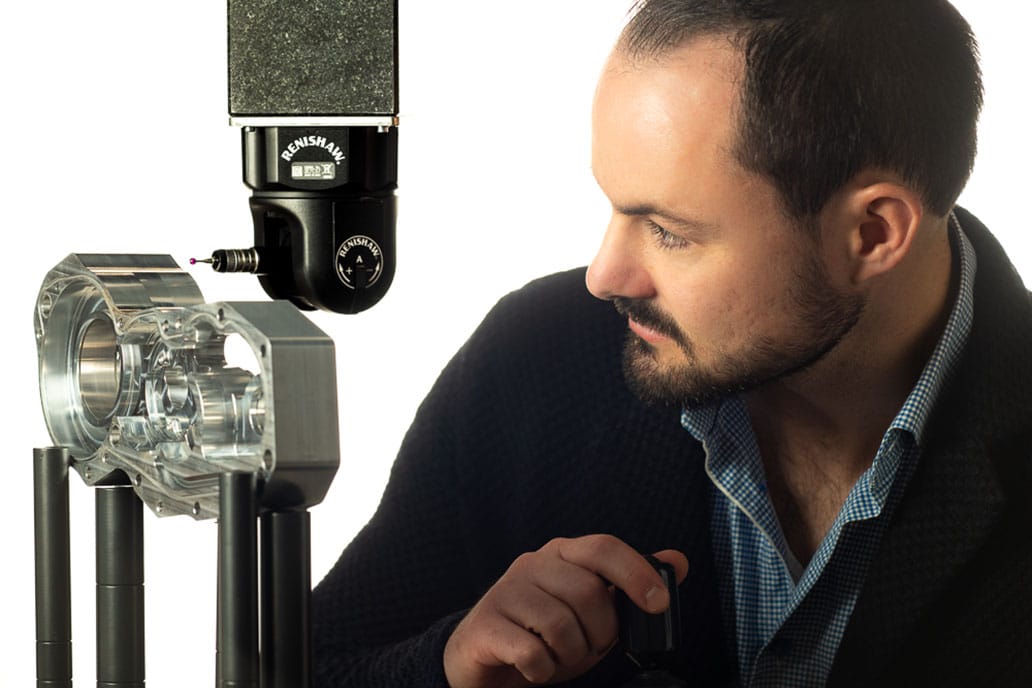 A man closely observes a Renishaw precision CMM inspecting a metal component.
