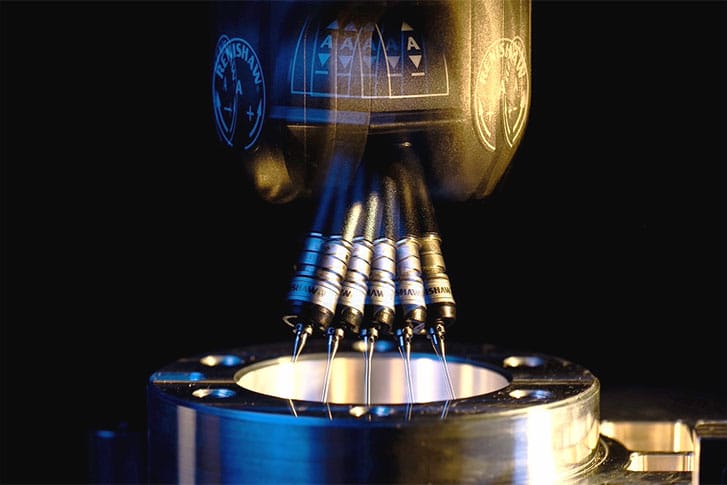 Close-up of a precision robotic machine with multiple nozzles injecting or assembling components into a metallic circular structure, illuminated by blue and yellow lighting for a high-tech industrial aesthetic.